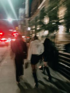 people walking down the street at night with their backs turned to the camera as cars pass by