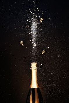 a bottle of champagne is being poured into the air with gold confetti sprinkles