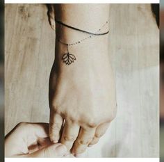 two hands holding each other with a flower tattoo on their left wrist and an ankle bracelet