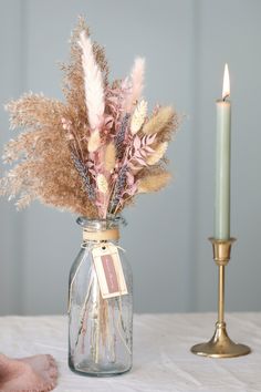 a vase filled with dried flowers next to a candle