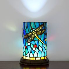 a stained glass lamp with a dragonfly on it's side sitting on a table