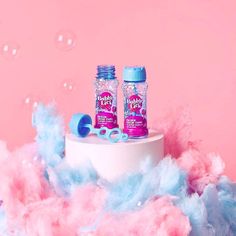 two pink and blue bottles sitting on top of a white table covered in foamy bubbles