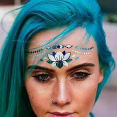 a woman with blue hair and face paint on her forehead, wearing a flower head piece