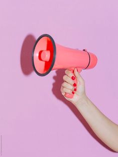 a woman's hand holding a pink and red megaphone on a pink background