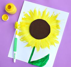 a sunflower painted on paper next to some yellow paint and a crayon marker