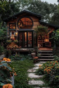 a small wooden house surrounded by greenery and orange flowers in the foreground, with stairs leading up to it