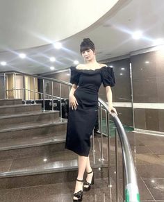 a woman in a black dress standing on some stairs