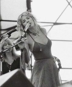 a woman in a dress holding a microphone up to her ear while standing on stage