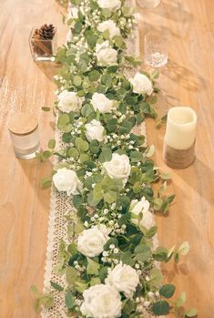 a long table with white flowers and greenery on the runner, along with candles