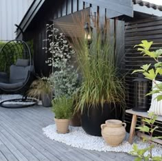 a wooden deck with potted plants next to a chair and other outdoor furniture on it