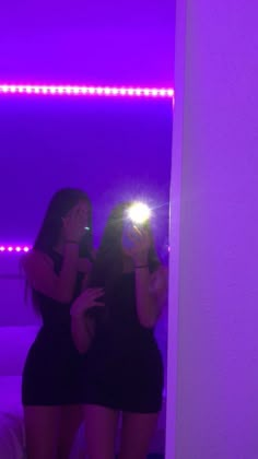 two women are standing in front of a mirror and one is holding a cell phone