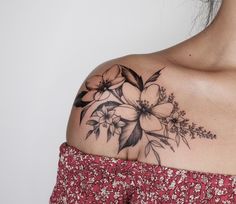 a woman's shoulder with flowers and leaves tattooed on the back of her shoulder