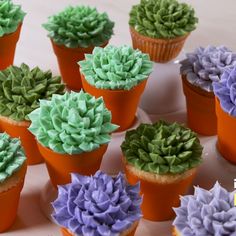 cupcakes with green and purple frosting in small pots on a table next to each other