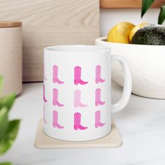 a white mug with pink cowboy boots on it next to a bowl of lemons