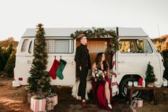 a man and woman standing in front of a white van with christmas stockings on it