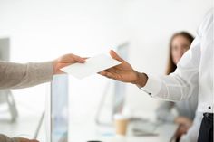 two business people shaking hands over a piece of paper in an office setting with one person sitting at a desk and the other standing behind them