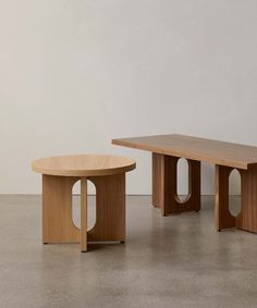 two wooden tables sitting next to each other on top of a cement floor in front of a white wall