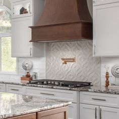 a kitchen with white cabinets and marble counter tops, an oven hood over the stove