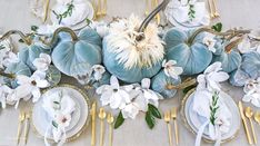 the table is set with blue and white flowers, gold chargers, and silverware