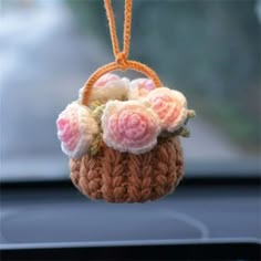 a small crocheted basket with flowers hanging from it's side in a car