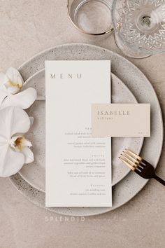 a table setting with white flowers and silverware on it, including a menu card