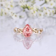 a pink diamond ring sitting on top of a white surface with flowers in the background