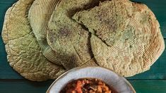 some breads and a bowl of food on a green wooden table with a blue background