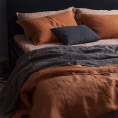 a bed with orange and black linens in a dark colored room, it is made up