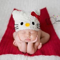 a baby wearing a hello kitty hat laying on top of a red and white blanket