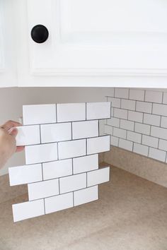 a person is placing white tiles on the wall