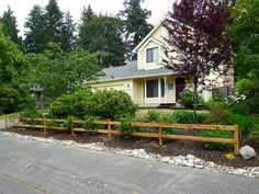 a yellow house sitting next to a lush green tree filled forest in front of a wooden fence