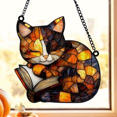 a stained glass cat reading a book on a window sill hanging from a chain