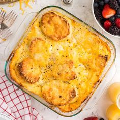 a casserole dish with meat and cheese on top next to berries, oranges, and forks