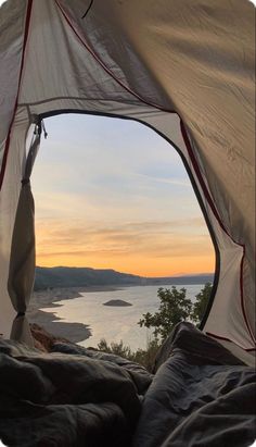 an open tent with the sun setting over water and mountains in the distance, as seen from inside it