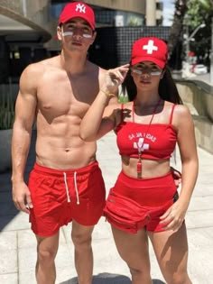 a man and woman in red bathing suits posing for a photo on the sidewalk with one another