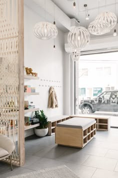 a white room with lots of hanging lights above the couches and tables in front of a large window