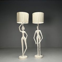 two white ceramic figurines with lamps on top of them, one holding a lamp and the other standing