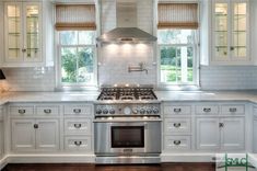 a kitchen with white cabinets and stainless steel stove top oven in front of two windows