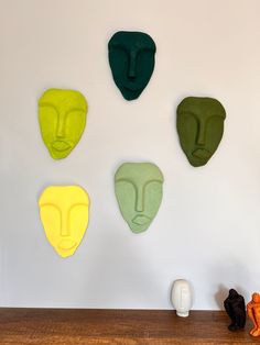 four different colored masks mounted on the wall above a wooden table with an orange and black cat