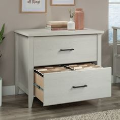 two drawers in a room with a plant on the floor next to it and framed pictures above them