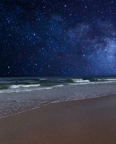 the night sky is filled with stars above the ocean and waves crashing on the beach