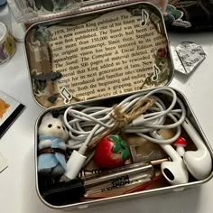 an open tin with various items in it sitting on a table next to other objects