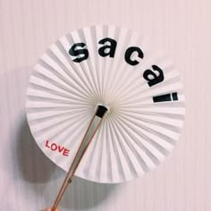 a hand holding a white paper fan with the word love written on it that says sasa