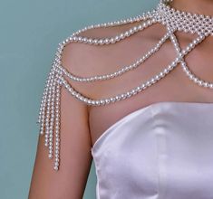 the back of a woman's white dress with pearls and chains on her shoulder