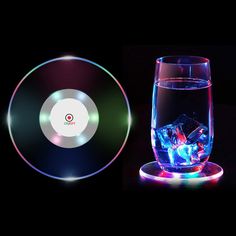 a glass with ice in it next to an illuminated cd disc on a black background