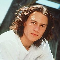 a close up of a person wearing a white shirt and posing for a photo with long curly hair