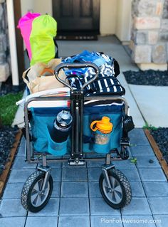 a baby stroller with various items in it sitting on the side walk next to a house