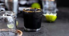 two glasses filled with black liquid and limes next to each other on a table