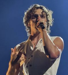 a man with curly hair holding a microphone in his hand and singing into the microphone