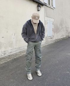 a man standing in front of a white building wearing a hat and grey sweatpants